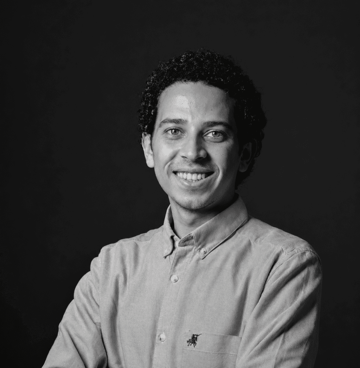 Black and white portrait of Anas Adel smiling, arms crossed